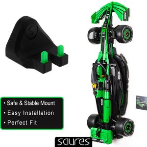 Peut inclure: Un support mural noir et vert pour voiture de course Lego avec deux languettes vertes sur le côté. Le support est conçu pour maintenir une voiture de course Lego en position verticale. Le texte "KICK" est imprimé sur la voiture. Le texte "Montage sûr et stable", "Installation facile" et "Ajustement parfait" est imprimé sous l'image.