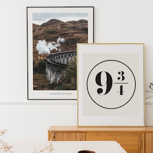 Könnte beinhalten: Zwei gerahmte Drucke auf einem Holzregal. Der Druck links zeigt einen Zug auf einer Brücke mit Bergen im Hintergrund. Der Druck rechts zeigt einen schwarzen Kreis mit der Zahl 9 und 3/4 darin. Der Text "HOGWARTS EXPRESS" befindet sich unter dem Bild links.