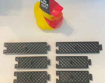 Puede incluir: Seis piezas de pista de plástico negro con un patrón de diamante. Las piezas están diseñadas para conectarse entre sí para crear una pista para un coche o tren de juguete.
