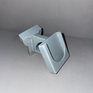 May include: A gray plastic U-shaped bracket with a rectangular base. The bracket has a hole in the center of the base.