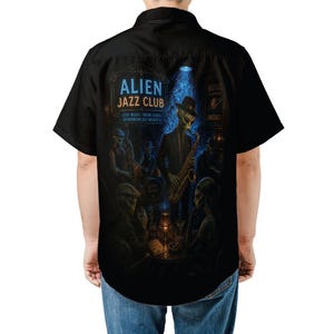 Puede incluir: Camisa negra de manga corta con una ilustración detallada de una escena de club de jazz alienígena. El diseño incluye músicos, un saxofonista y el texto "Alien Jazz Club". La camisa tiene un cuello clásico.