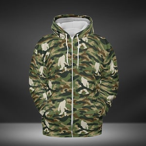 May include: A green, brown, and white camouflage print zip-up hoodie with a silhouette of a Bigfoot walking across the fabric.