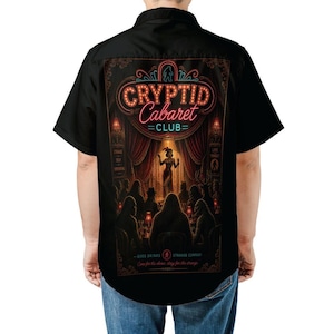 Puede incluir: Camisa negra con un diseño de Cryptid Cabaret Club en la espalda. El gráfico incluye un letrero de neón, un escenario con una artista y una audiencia. El texto dice "Good Drinks, Strange Company, Come for the show, stay for the strange."