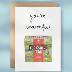 May include: A white greeting card with a brown envelope featuring a hand-drawn illustration of a box of Yorkshire Tea. The text above the box reads you're tea-rrific! The box illustration includes green hills, a small sheep, and the text 250g.