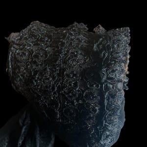 Puede incluir: Un gorro de encaje negro con un borde rizado. El gorro est&aacute; hecho de encaje delicado e intrincado y tiene un drapeado suave y fluido.