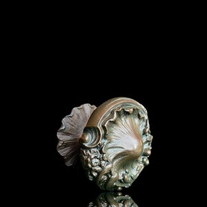 Op de afbeelding: Een vintage bronzen deurklink met een sierlijk ontwerp met een schelpvorm en bloemmotieven.