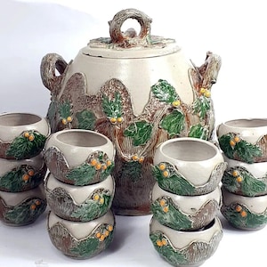 Può includere: Un set di ciotole da portata in ceramica con un design rustico e boschivo. Le ciotole sono impilate e presentano uno schema di colori marrone, verde e bianco con un motivo a foglie. Il set include una grande ciotola da portata con coperchio dal design simile.