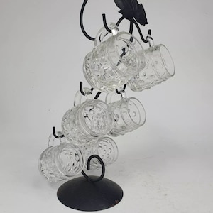 May include: A black metal wine glass rack shaped like a grapevine with eight clear glass mugs hanging from it.