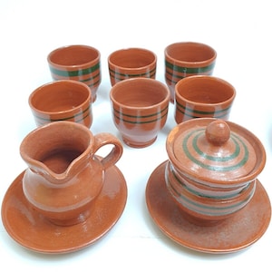 Könnte beinhalten: Ein Set aus braunen Tonbechern und einem Krug mit grünen Streifen. Das Set enthält eine Zuckerdose mit Deckel und eine Untertasse.