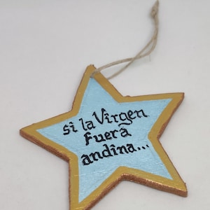 May include: A blue star-shaped ornament with a gold border and a handwritten message in Spanish that reads "si la Virgen fuera andina..."
