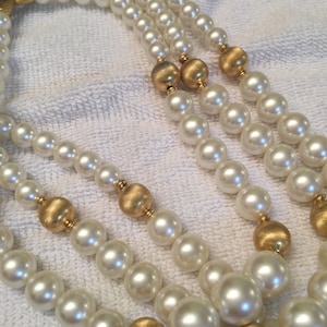 May include: A three-strand pearl necklace with gold accents. The pearls are white and the gold accents are round.