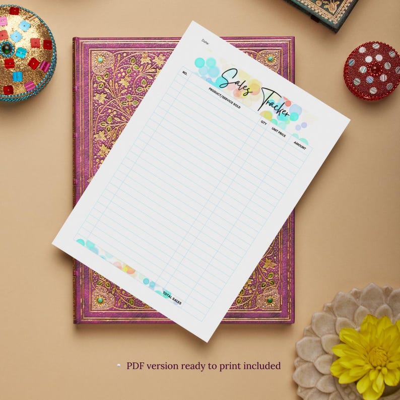 May include: A white sales tracker sheet with a colorful bubble design and the words "Sales Tracker." The sheet is on a purple journal with gold floral designs. The words "PDF version ready to print included" are at the bottom.