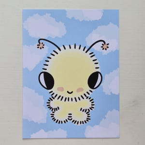 May include: A rectangular art print featuring a pale yellow, fuzzy creature with large black eyes, antennae, and pink cheeks. The creature is centred against a light blue background filled with soft, white, fluffy clouds in a sky-like pattern.