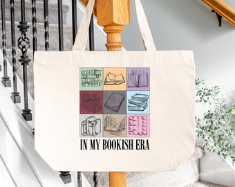 May include: A natural canvas tote bag with a colourful book-themed design. The design features nine squares with illustrations of books and the text "IN MY BOOKISH ERA". The bag has two long handles.
