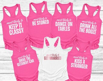 May include: Set of seven pink and white tank tops with humorous text printed on the front. The text reads "most likely to" followed by a different phrase on each tank top. The phrases are "keep it classy", "be stoned", "dance on tables", "drink all the booze", "drive the getaway car", "get married", and "kiss a stranger".