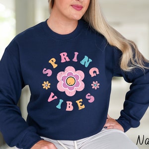 Op de afbeelding: Navyblauwe trui met een bloemenprint en de tekst "Spring Vibes" in een retro-lettertype.