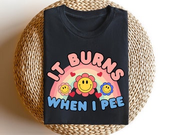 May include: Black t-shirt with a rainbow and smiley faces graphic. The text "It burns when I pee" is printed in blue.