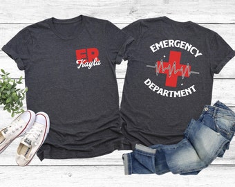 May include: Two dark heather grey t-shirts with a red and white graphic design. The front shirt has the letters "ER" in red with the name "Kayla" underneath. The back shirt has a red cross with a heartbeat line and the words "Emergency Department".