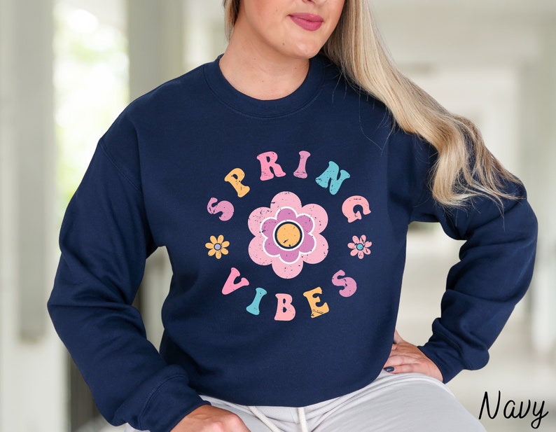 Op de afbeelding: Navyblauwe trui met een bloemenprint en de tekst "Spring Vibes" in een retro-lettertype.