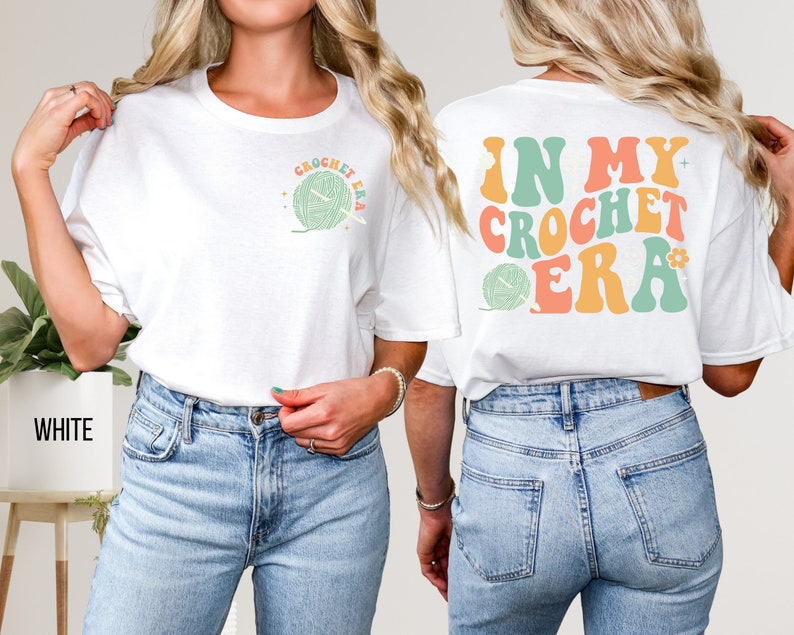 K&ouml;nnte beinhalten: Wei&szlig;es T-Shirt mit dem Text "CROCHET ERA" und einer Garnkn&auml;uel-Grafik auf der Vorderseite. Auf der R&uuml;ckseite des Shirts steht der Text "IN MY CROCHET ERA" in Retro-Farben. Ein lustiges, l&auml;ssiges Oberteil f&uuml;r Handwerker.