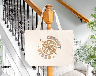 May include: A natural canvas tote bag with a colorful graphic of a yarn ball and crochet hook. The text "CROCHET VIBES" is written around the graphic.