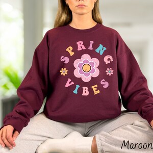 Op de afbeelding: Maroon sweatshirt met een grafische print van een bloem en de tekst "Spring Vibes" in kleurrijke letters.