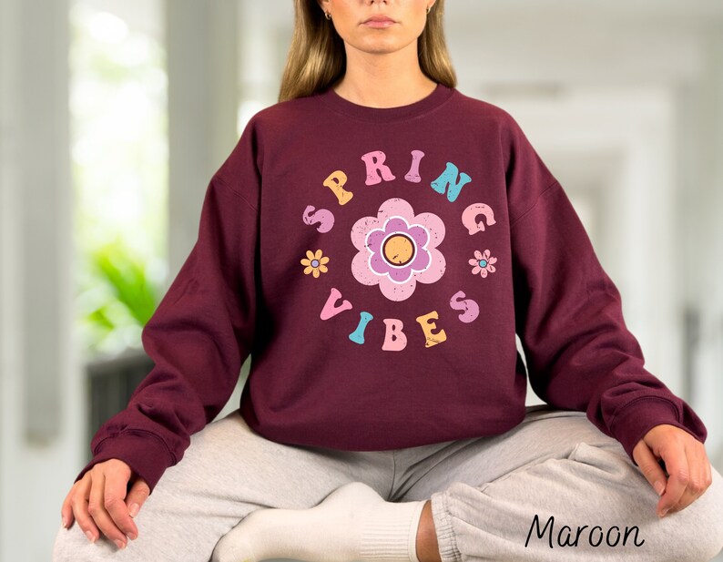 Op de afbeelding: Maroon sweatshirt met een grafische print van een bloem en de tekst "Spring Vibes" in kleurrijke letters.