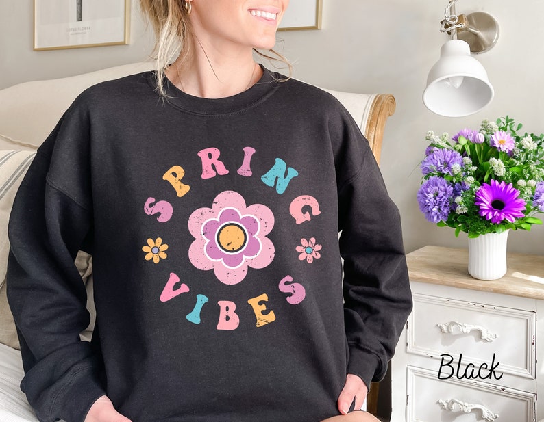 Op de afbeelding: Zwart sweatshirt met een grafische print van een bloem en de tekst "SPRING VIBES" in kleurrijke letters.