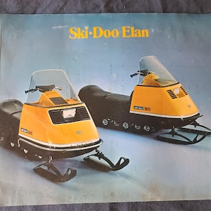 May include: A vintage brochure showcasing two yellow and black Ski-Doo Elan snowmobiles. The snowmobiles have a distinctive design with a windshield, black seats, and skis. The brochure has the words "Ski-Doo Elan" in gold lettering.
