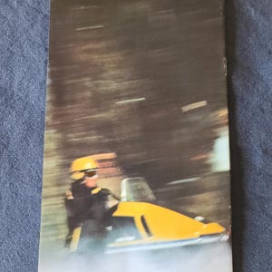 May include: Vintage advertisement featuring a yellow snowmobile in motion. The driver wears a yellow helmet and dark clothing. The background is blurred, suggesting speed. Text at the bottom reads "Litho'd in Canada" and "T.M. Bombardier Limited &copy; Sept. 1969 480 3019."