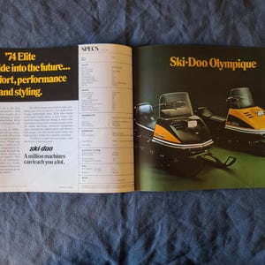 May include: A vintage magazine spread showcasing two Ski-Doo snowmobiles. The left page features yellow text: "'74 Elite Take a ride into the future... of comfort, performance and styling." The right page displays "Ski-Doo Olympique" in yellow.