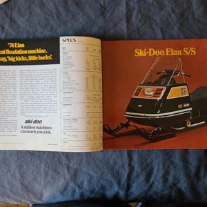 May include: A magazine spread showcasing a vintage Ski-Doo Elan S/S snowmobile. The snowmobile is black with orange detailing and the letters "SS". The page includes text about the snowmobile and the "ski-doo" brand.