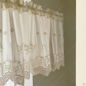 May include: Cream-coloured lace curtain with floral embroidery and scalloped edges. The curtain features a ruffled top and delicate, embroidered flowers and vines. The design is a mix of solid fabric and openwork lace, creating a light and airy feel.