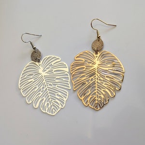 Puede incluir: Un par de pendientes de oro y plata con un dise&ntilde;o de hoja. Los pendientes est&aacute;n hechos de metal y tienen un patr&oacute;n delicado e intrincado.