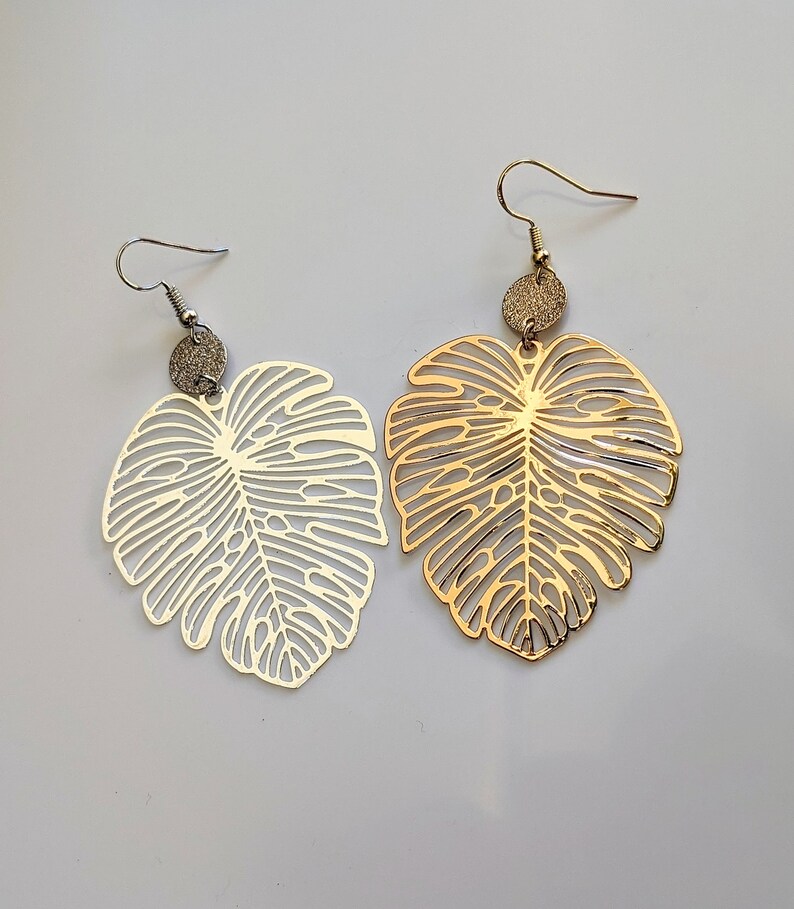 Puede incluir: Un par de pendientes de oro y plata con un dise&ntilde;o de hoja. Los pendientes est&aacute;n hechos de metal y tienen un patr&oacute;n delicado e intrincado.