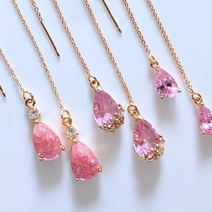 Könnte beinhalten: Fünf Paare rosa Ohrringe mit goldenen Ketten. Zwei Paare haben rosa tropfenförmige Steine mit einem glitzernden Finish. Die anderen drei Paare haben rosa tropfenförmige Steine mit einem glatten Finish.