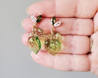 May include: A pair of gold earrings with green and clear glass leaves. The leaves are layered and have a delicate, organic look.