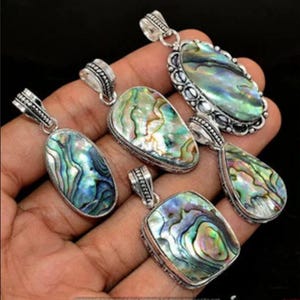Könnte beinhalten: Fünf silberne Anhänger mit Einlagen aus Abalone-Schale. Die Anhänger haben verschiedene Formen, darunter oval, tropfenförmig und quadratisch. Die Abalone-Schale hat schillernde Farben in Grün, Blau und Lila.