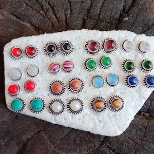 May include: A collection of 20 pairs of silver stud earrings with various colored gemstones. The earrings are displayed on a white foam surface.