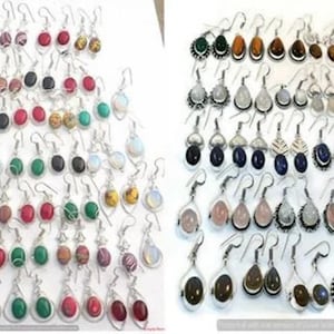 Könnte beinhalten: Eine große Sammlung von silbernen Ohrringen mit verschiedenen Edelsteinfarben, darunter Rot, Grün, Blau, Schwarz und Weiß. Die Ohrringe sind in zwei Reihen auf weißem Hintergrund angeordnet.