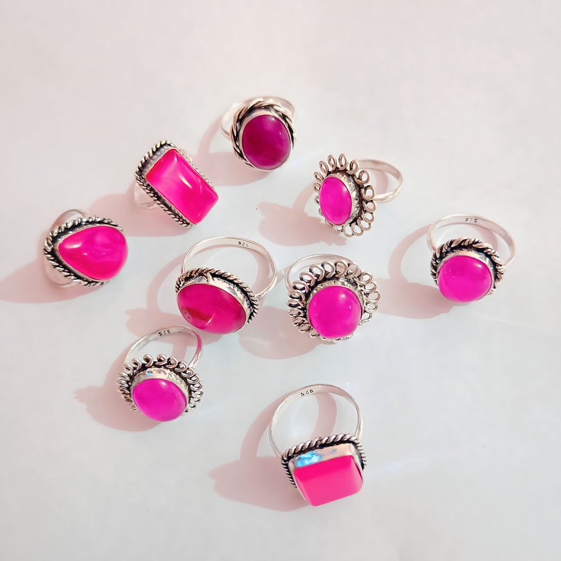 May include: Nine silver rings with pink gemstone settings. The rings have different styles of bands and settings. Some rings have a square setting, some have a round setting, and some have a more ornate setting.