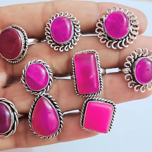 May include: Nine silver rings with pink and red gemstones. The rings have different styles of settings, including round, oval, and square.
