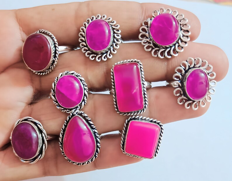 May include: Nine silver rings with pink and red gemstones. The rings have different styles of settings, including round, oval, and square.