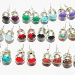 May include: A set of 18 silver stud earrings with various colored gemstones. The gemstones include red, blue, green, purple, black, white, and multi-colored.