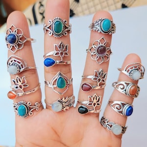 Puede incluir: Una colección de anillos de plata con varias piedras preciosas, incluyendo turquesa, lapislázuli, piedra lunar y cornalina. Los anillos presentan diseños intrincados, como flores de loto, hojas y espirales.