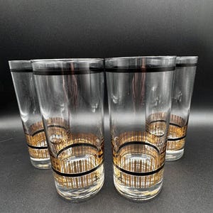 May include: Set of five clear highball glasses with black rims and gold and black patterned bands around the base. The glasses are tall and cylindrical, perfect for serving cocktails or other beverages.