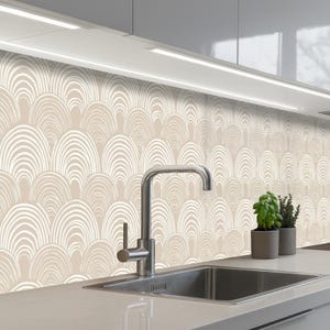 Peut inclure: Un fond de cuisine avec un motif répétitif de formes arquées blanches sur un fond beige. Un robinet et un évier en acier inoxydable sont au premier plan, avec de petites plantes en pot à droite. Le design crée une esthétique moderne et épurée.