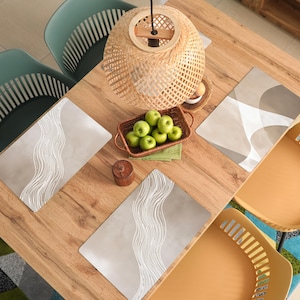 Peut inclure: Une table à manger en bois avec quatre chaises, des sets de table et une suspension en osier. La table est dressée avec quatre sets de table avec un motif de vagues, un panier de pommes vertes et un petit bougeoir en bois.