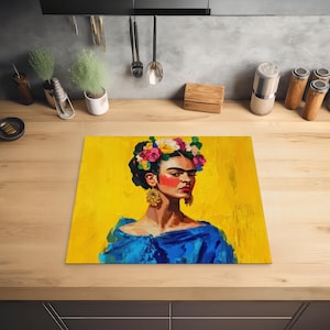 Peut inclure: Un dessous-de-plat rectangulaire jaune représentant un portrait de Frida Kahlo. L'œuvre d'art représente Kahlo avec une couronne de fleurs, du fard à joues rouge et des boucles d'oreilles dorées. Elle porte un haut bleu sur fond jaune.