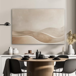 May include: A large, rectangular abstract canvas art piece with a neutral color palette of beige and brown tones. The artwork features a layered, wave-like design. The image also shows a dining table set with black chairs, plates, and decorative items.
